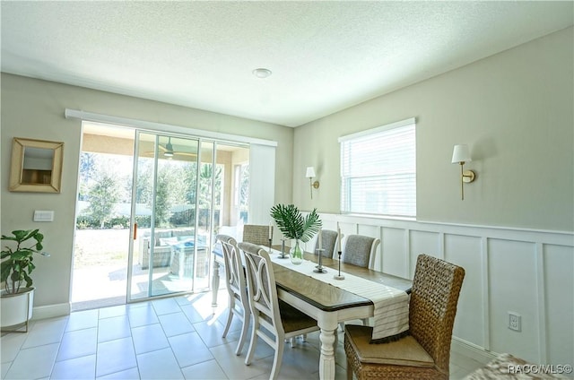 dining space featuring a textured ceiling, a healthy amount of sunlight, wainscoting, and a decorative wall