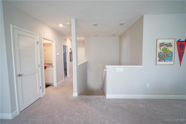 hall with an upstairs landing, light colored carpet, and baseboards