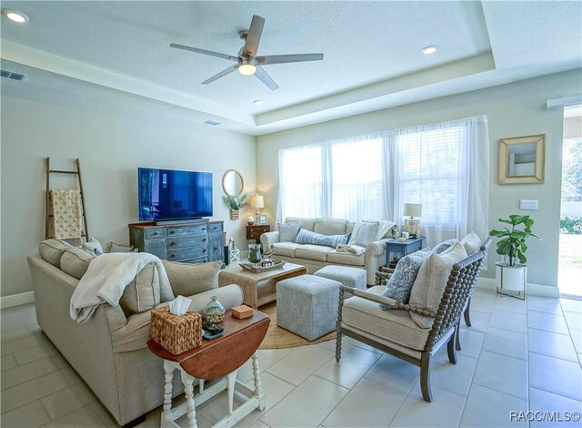 living area featuring a tray ceiling, baseboards, visible vents, and light tile patterned flooring