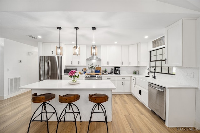 kitchen with a center island, hanging light fixtures, stainless steel appliances, light hardwood / wood-style floors, and white cabinets