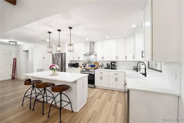 kitchen with appliances with stainless steel finishes, wall chimney exhaust hood, sink, white cabinets, and a center island