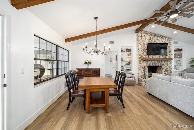 dining area with lofted ceiling with beams, a stone fireplace, ceiling fan with notable chandelier, and light hardwood / wood-style flooring