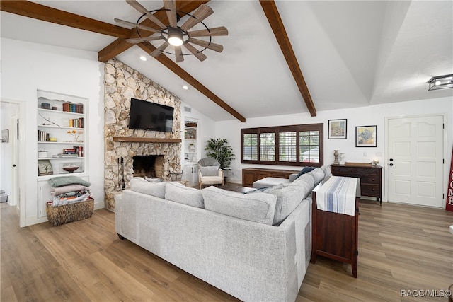 living room with built in shelves, ceiling fan, vaulted ceiling with beams, a stone fireplace, and light hardwood / wood-style flooring