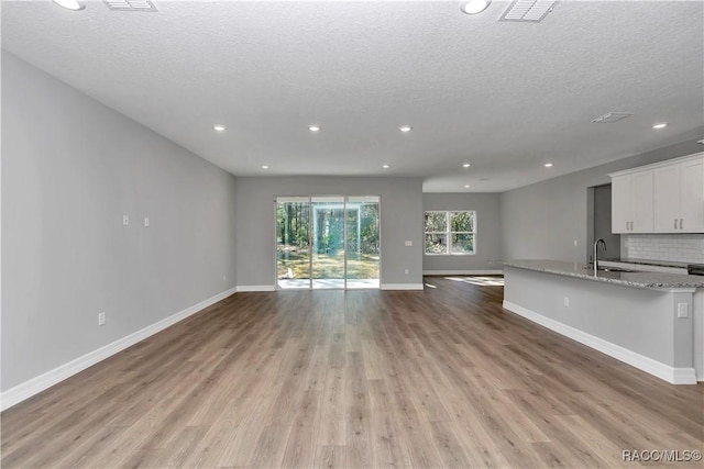 unfurnished living room with sink, a textured ceiling, and light hardwood / wood-style flooring