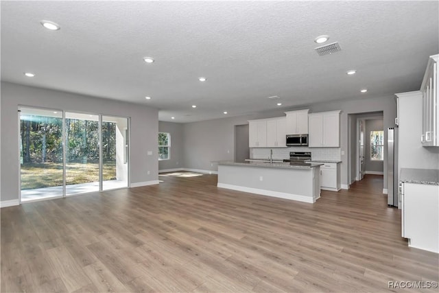 kitchen featuring a center island with sink, appliances with stainless steel finishes, white cabinets, light stone counters, and sink