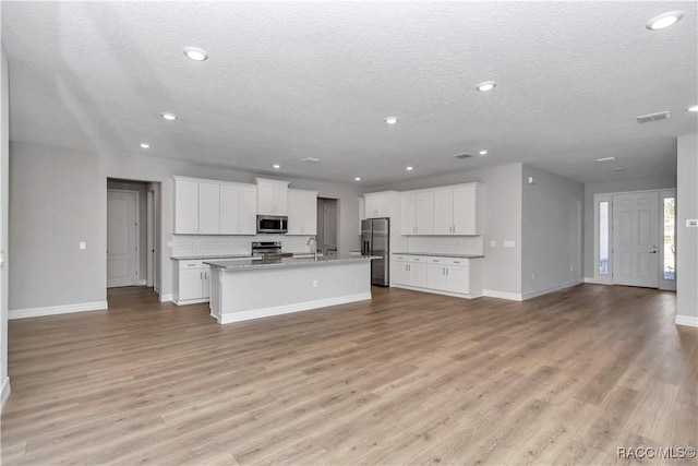 kitchen with white cabinets, backsplash, an island with sink, and stainless steel appliances