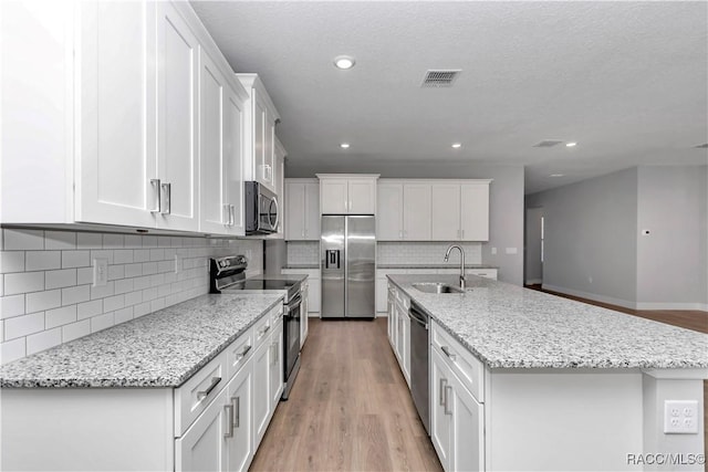 kitchen with appliances with stainless steel finishes, sink, white cabinetry, and a center island with sink