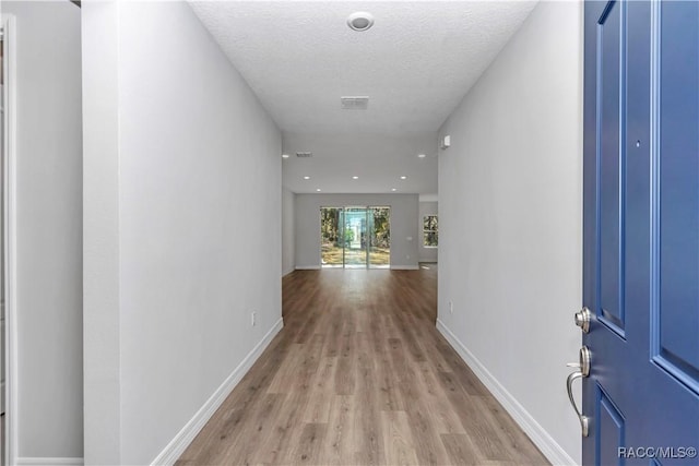 hallway with light hardwood / wood-style floors and a textured ceiling