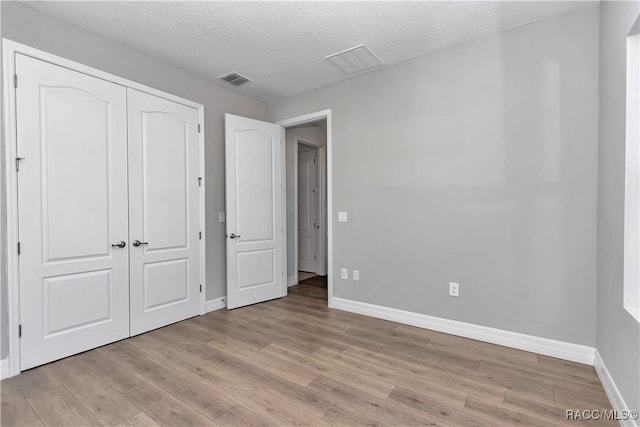 unfurnished bedroom featuring a textured ceiling, a closet, and light hardwood / wood-style floors