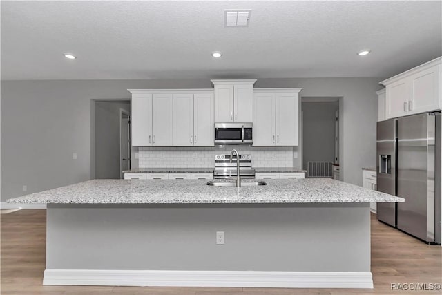 kitchen with appliances with stainless steel finishes, white cabinetry, tasteful backsplash, sink, and a center island with sink