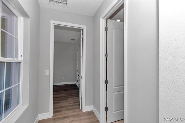 corridor with light wood-type flooring and a textured ceiling