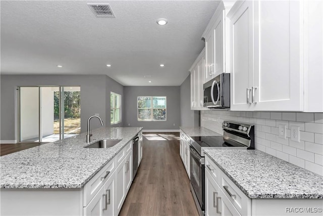 kitchen with an island with sink, stainless steel appliances, white cabinets, light stone counters, and sink