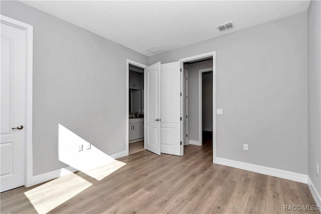 unfurnished bedroom featuring ensuite bathroom and light hardwood / wood-style flooring