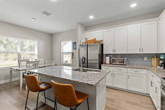 kitchen featuring white cabinetry, decorative backsplash, light stone counters, stainless steel fridge with ice dispenser, and a center island with sink