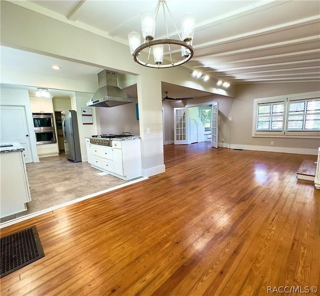 unfurnished living room featuring ceiling fan with notable chandelier, beam ceiling, and light wood-type flooring