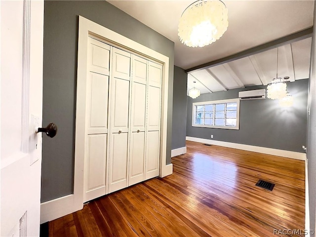 unfurnished bedroom featuring vaulted ceiling with beams, dark hardwood / wood-style floors, an AC wall unit, and a closet