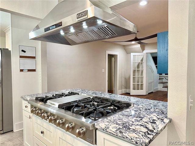 kitchen featuring white cabinetry, light stone counters, wall chimney range hood, and appliances with stainless steel finishes