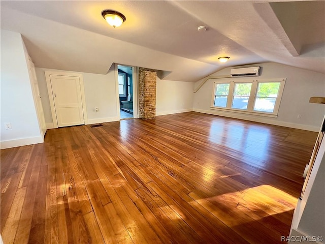 additional living space featuring wood-type flooring, vaulted ceiling, and an AC wall unit