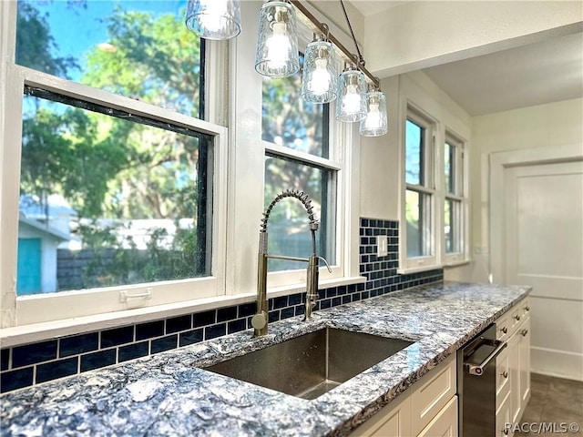 kitchen with white cabinetry, sink, light stone counters, backsplash, and pendant lighting