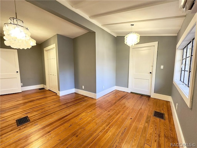 interior space with a wall mounted air conditioner, lofted ceiling with beams, light hardwood / wood-style floors, and an inviting chandelier