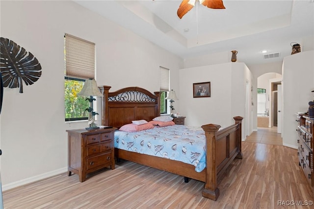 bedroom featuring light hardwood / wood-style floors, multiple windows, a tray ceiling, and ceiling fan