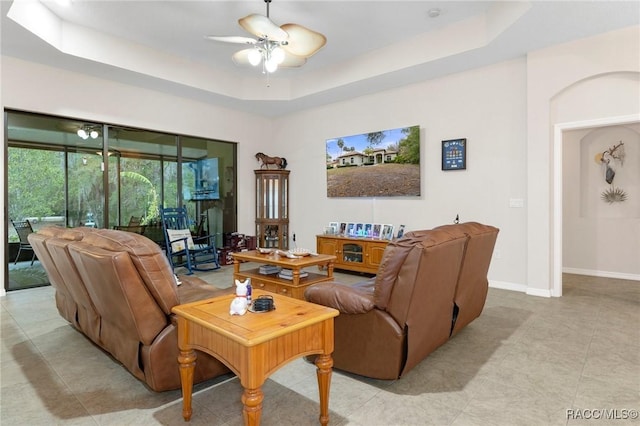 living room featuring ceiling fan, light tile patterned floors, and a tray ceiling