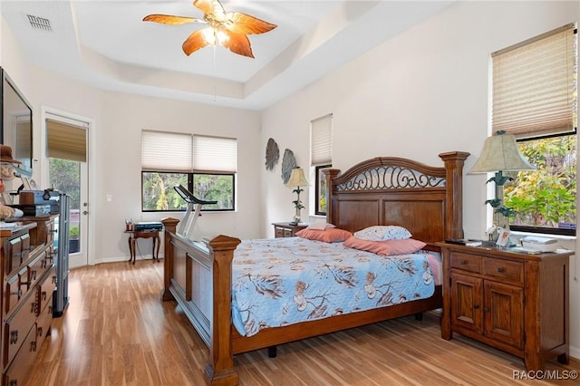 bedroom with ceiling fan, light hardwood / wood-style flooring, and a tray ceiling