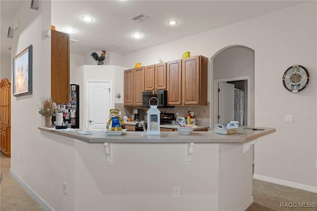 kitchen featuring a breakfast bar, light tile patterned floors, kitchen peninsula, and stove