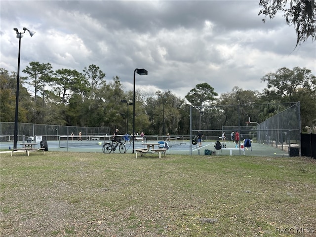 view of community featuring a tennis court, fence, and a yard