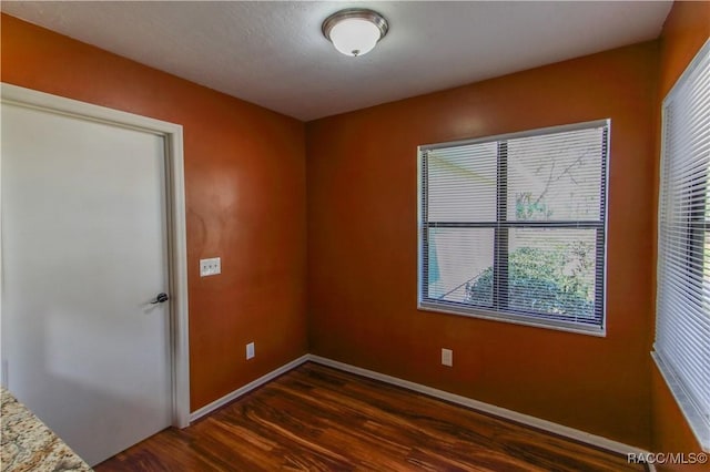 spare room featuring dark wood-style floors and baseboards