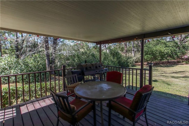 deck with outdoor dining space, a lawn, and a grill