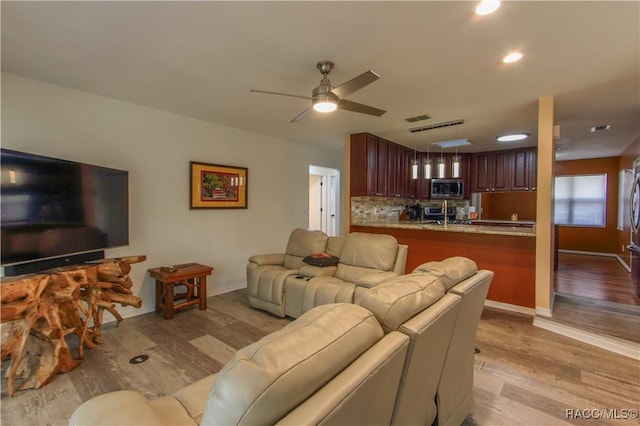 living room featuring light wood-style floors, visible vents, baseboards, and a ceiling fan