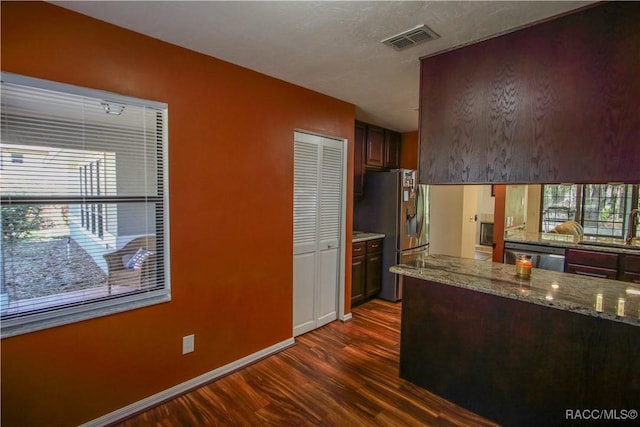 kitchen with stainless steel appliances, visible vents, light stone counters, and dark wood-type flooring