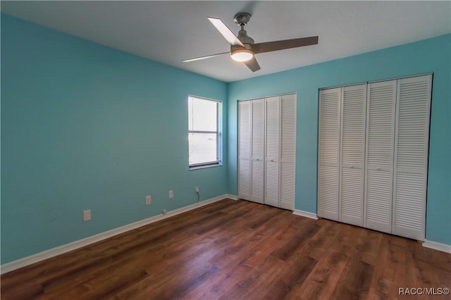 unfurnished bedroom with dark wood-style floors, two closets, a ceiling fan, and baseboards