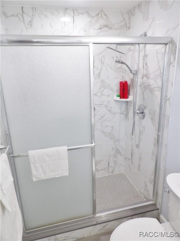 bathroom featuring a shower with shower door and toilet