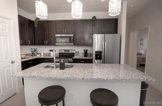 kitchen featuring hanging light fixtures, appliances with stainless steel finishes, a kitchen island with sink, and light stone counters