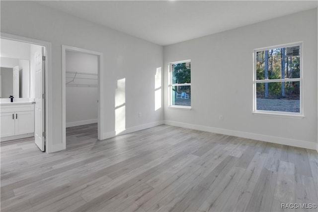 unfurnished bedroom with connected bathroom, a closet, a spacious closet, sink, and light hardwood / wood-style flooring