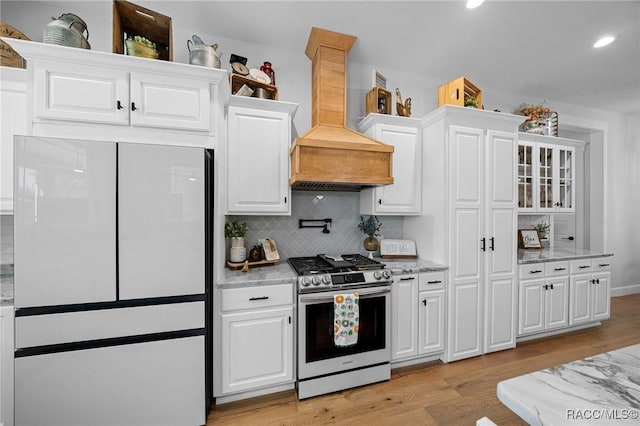 kitchen with white cabinets, range with gas cooktop, freestanding refrigerator, light wood-style floors, and premium range hood