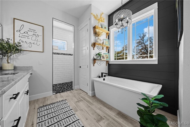 bathroom with a walk in shower, wood finished floors, vanity, baseboards, and a soaking tub