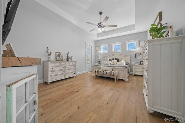 bedroom featuring light wood finished floors, baseboards, a tray ceiling, and a ceiling fan