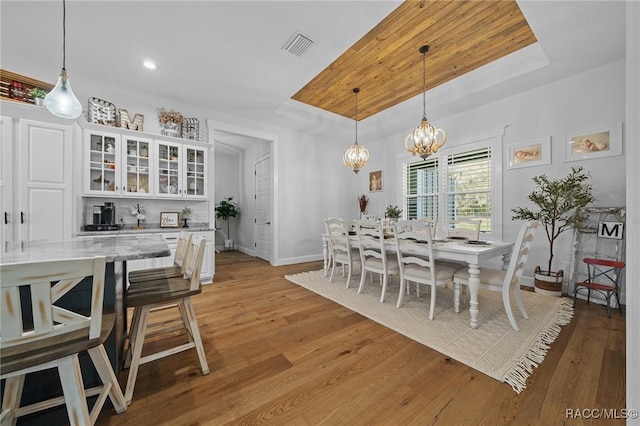 dining area with light wood-style floors, a raised ceiling, visible vents, and baseboards