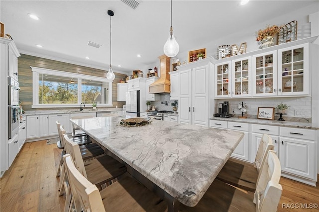 kitchen featuring appliances with stainless steel finishes, custom exhaust hood, white cabinetry, and light wood-style floors