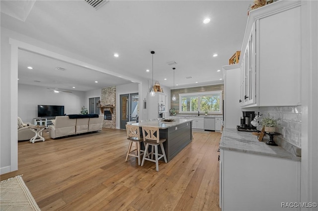 kitchen with a large fireplace, white cabinetry, decorative backsplash, and light wood-style floors