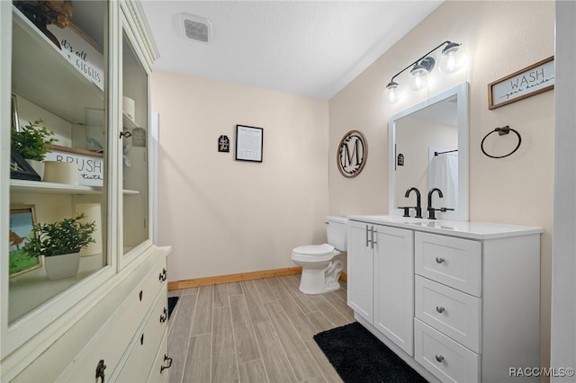 full bath featuring toilet, wood finished floors, visible vents, vanity, and baseboards