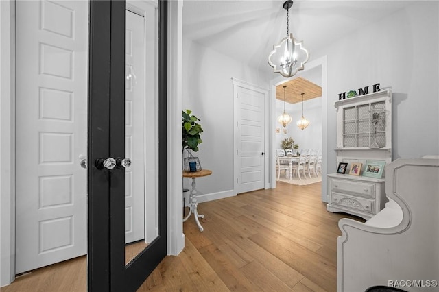 hallway featuring baseboards, light wood finished floors, and an inviting chandelier