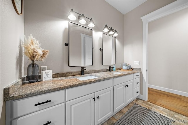 bathroom with double vanity, baseboards, a sink, and wood finished floors