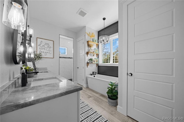 full bath featuring a garden tub, a notable chandelier, wood finished floors, a sink, and double vanity