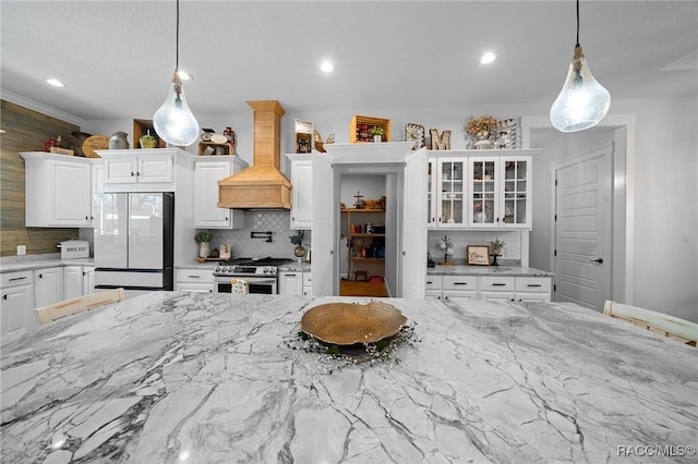 kitchen featuring premium range hood, white cabinetry, fridge, stainless steel gas stove, and glass insert cabinets