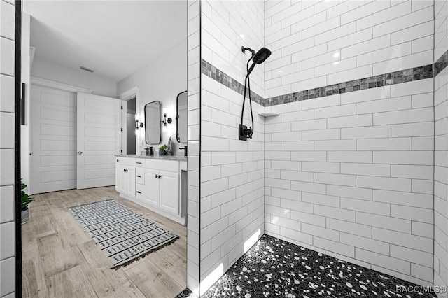 full bath featuring visible vents, tiled shower, wood finished floors, and vanity