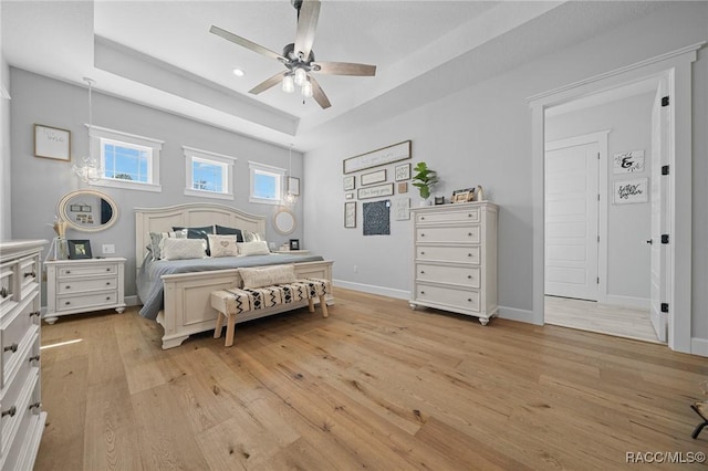 bedroom featuring light wood-style floors, a raised ceiling, baseboards, and a ceiling fan